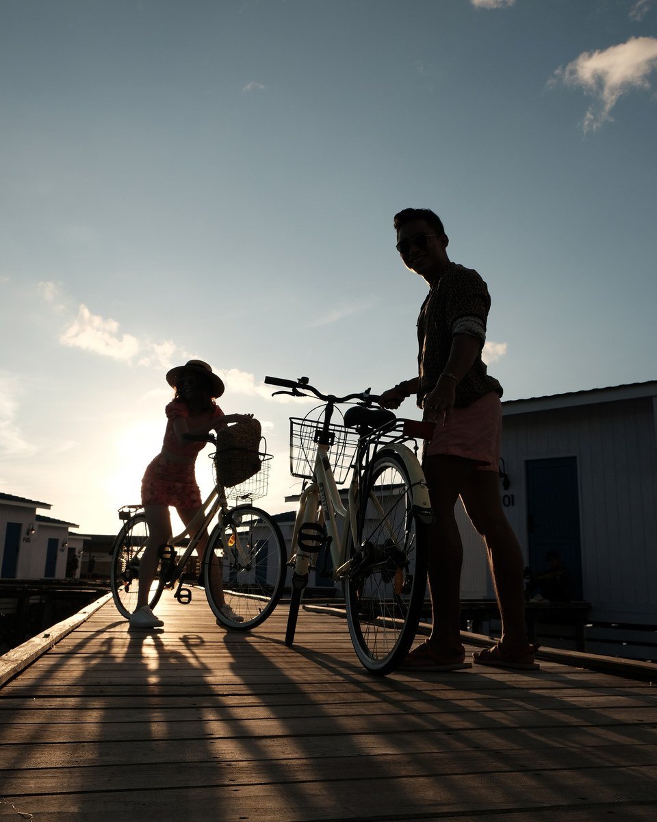 Two guests with bicycles on the Arasatu boardwalk in late-afternoon light.