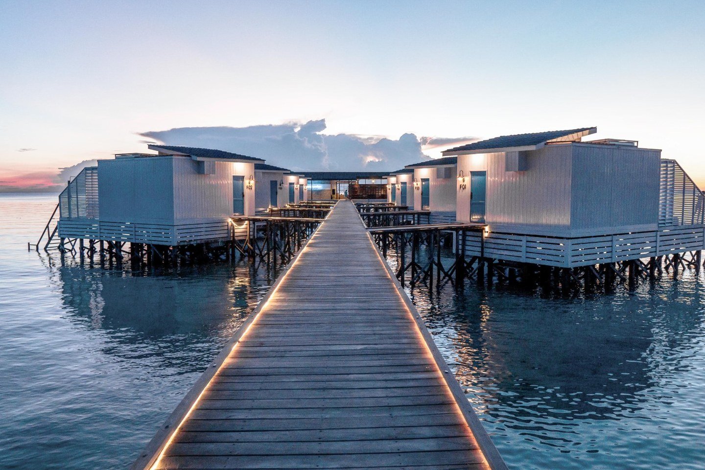 The illuminated boardwalk leading toward Arasatu's Floating Villas and Samamea at dusk.