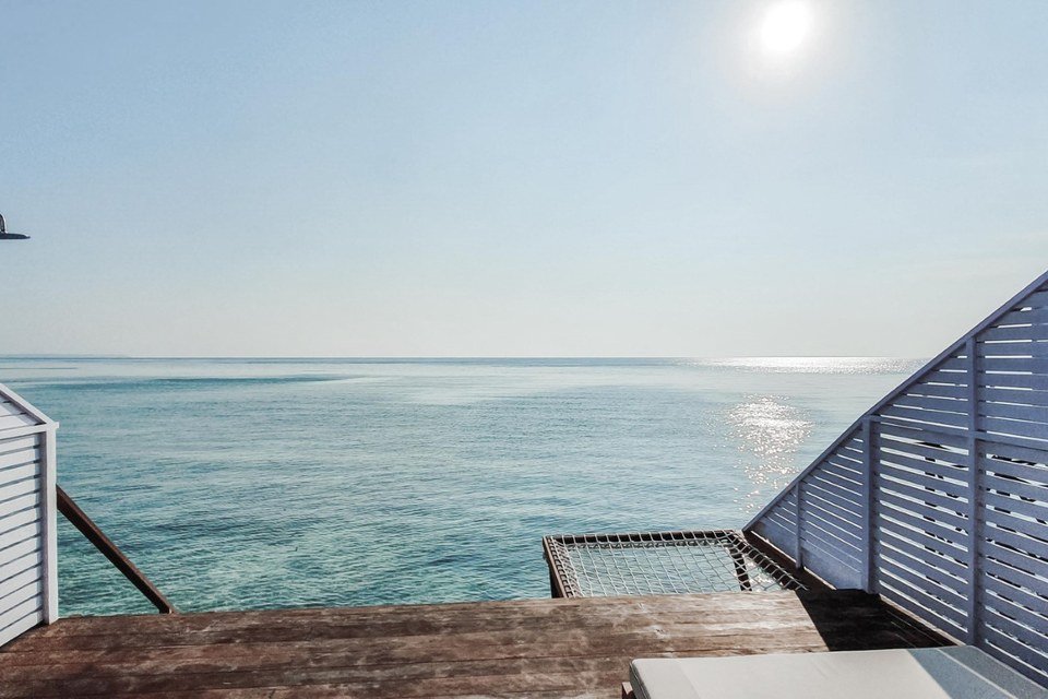 Furnished balcony of an Arasatu Floating Villa above coral-rich water.