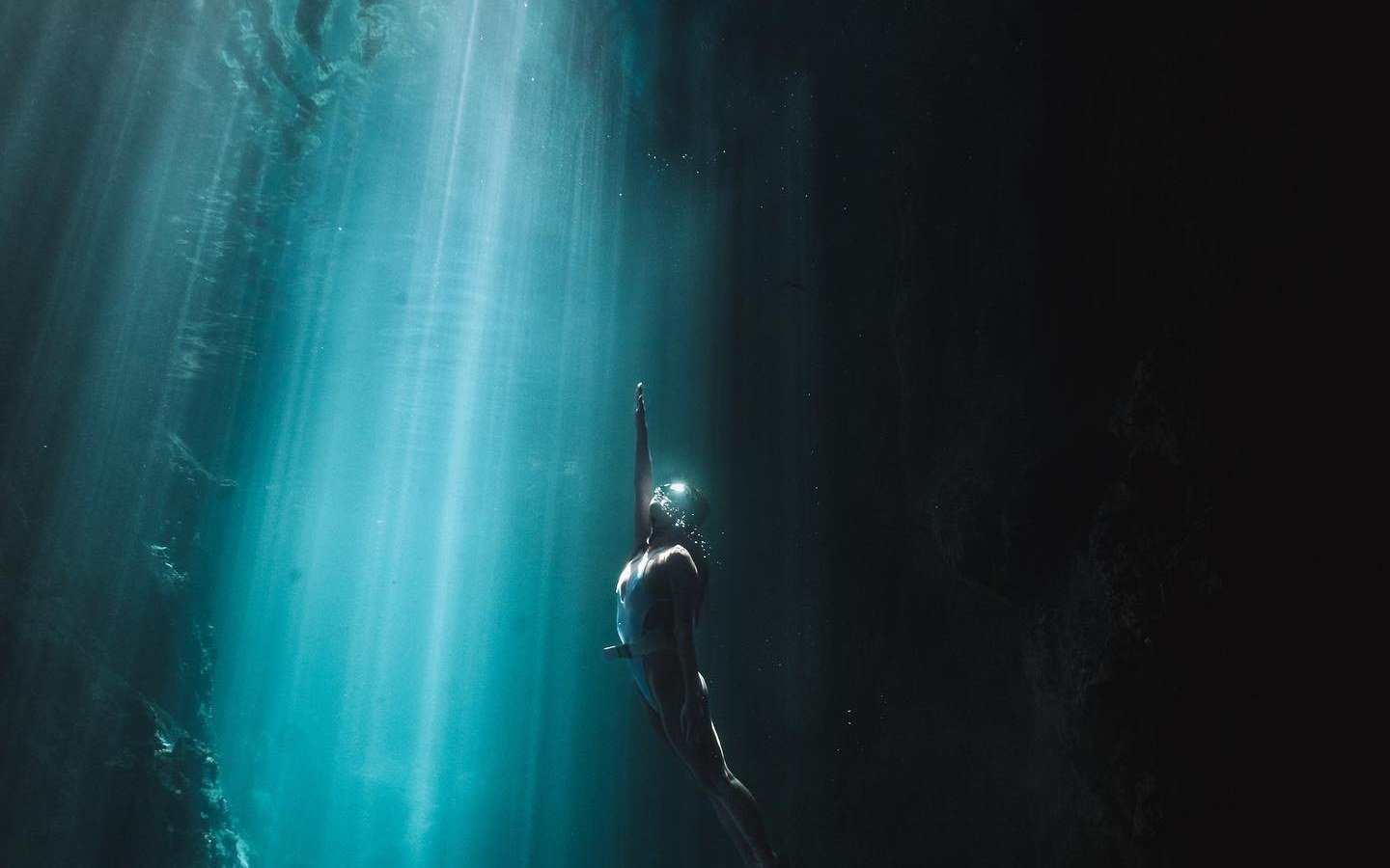 A swimmer beneath shafts of sunlight inside Halo Tabung Cave near Maratua.